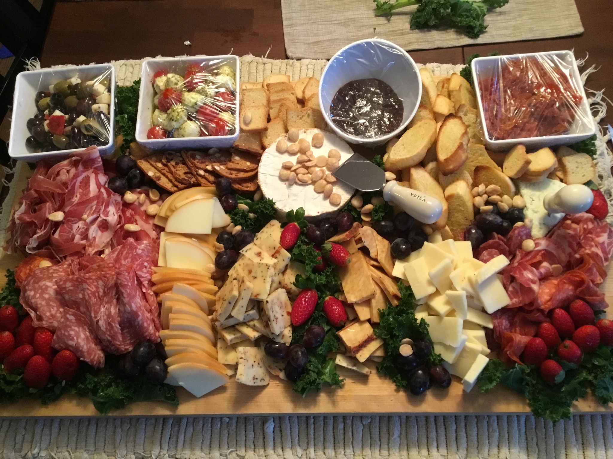 Large charcuterie and cheese board with meats, olives, crackers, grapes, and berries